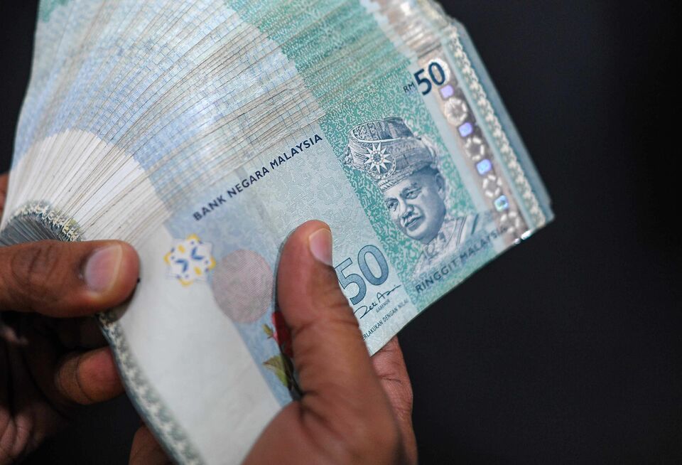 A money changer counts Malaysian ringgit banknotes for customers in Kuala Lumpur on June 11, 2015. (AFP Photo/Mohd Rasfan)