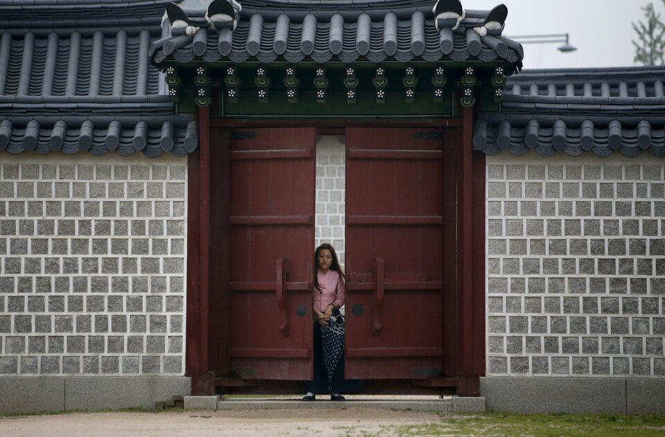 An employee in traditional costume stands behind a locked gate at Gyeongbok Palace in central Seoul. (Reuters Photo/Kim Hong-ji)