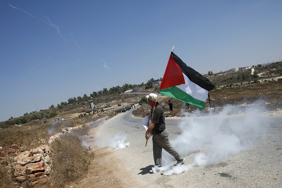 A Palestinian protester holds a Palestinian flag as he walks next to a tear gas canister fired by Israeli troops during clashes in the West Bank village of Nabi Saleh, near Ramallah, earlier this month. (Reuters Photo/Mohamad Torokman)