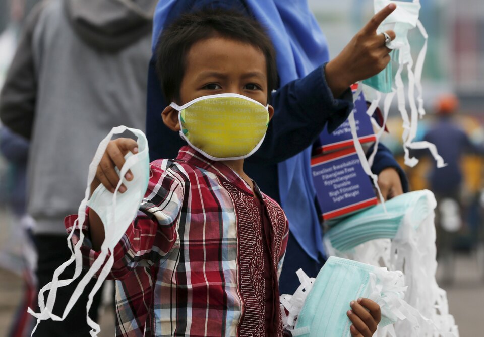 A child offers face masks to people along a haze shrouded street in Palembang, South Sumatra. (Reuters/Beawiharta)