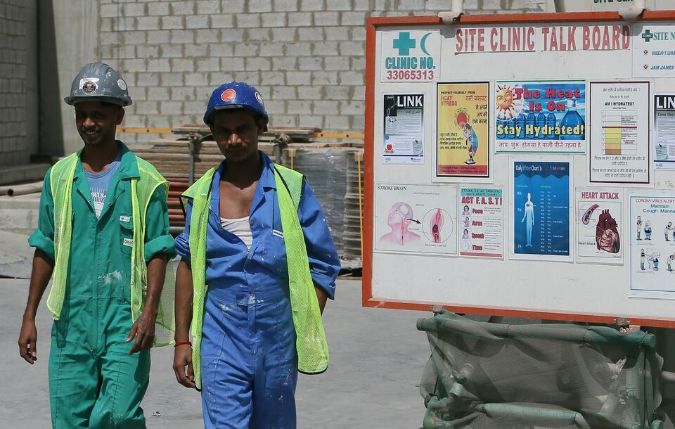 Migrant labourers walking past a board as they work on a construction site in Doha in Qatar. Rights groups on October 28, 2015 dismissed as a "sham" long-awaited reforms of Qatar