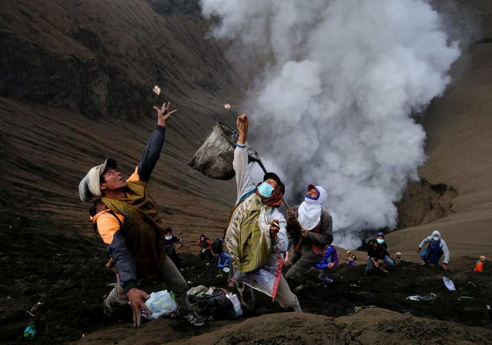 Villagers try to catch money thrown by worshipers as smoke and ash rise from Mount Bromo in East Java. (Reuters Photo/Beawiharta)