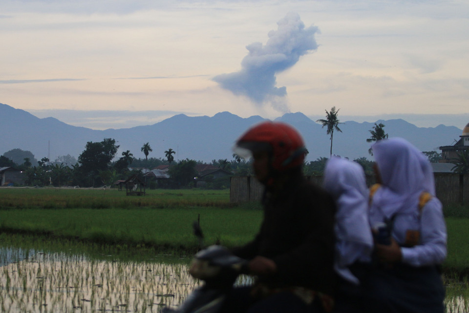 A motorcyclist drives in Sunggal as Mount Sinabung belches volcanic material in the backdrop, in North Sumatra, on Tuesday (19/07). The volcanic ash resulted from an eruption of the 2,460-meter-high volcano two weeks ago which also released incandescent lava, flowing as much as 1,000 meters down its eastern and southeastern slopes. (Antara Photo/Irsan Mulyadi)