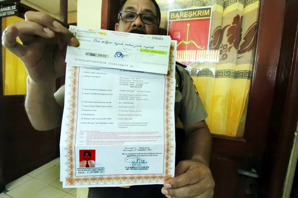 A police officer is pictured showing a fake check worth hundreds of millions of rupiah, a business license known as an SIUP and a land title certificate obtained by Banda Sakti Police after a victim lost Rp 40 million ($3039) in Lhokseumawe, Aceh, on Wednesday (03/08). Police are asking citizens to be careful of a new kind of scam where the perpetrator pretends to lose a brown envelope wrapped in plastic which contains forged checks and business licenses, which they then ask the person who finds the envelope — in this case the victim — to call the number listed on the license. The perpetrator, who pretends to be happy to have found his lost documents then asks for the finder's bank account number on the pretense that they want to send money to thank them, but instead they drain the victim's account. (Antara Photo/Rahmat)