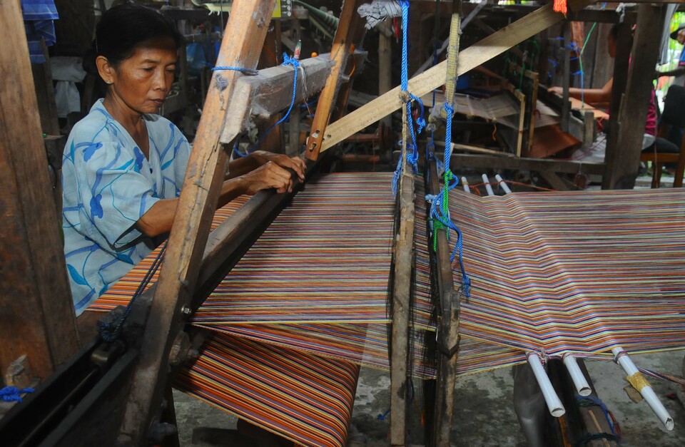A craftsman is pictured weaving yarn by hand to create striated fabric in Mlese, Cawas, Klaten, Central Java, on Wednesday (24/08). Central Statistics Agency (BPS) data showed there are currently 57.6 million small and medium enterprises operating in Indonesia, contributing to nearly 60 percent of the country's gross domestic product. (Antara Photo/Aloysius Jarot Nugroho)