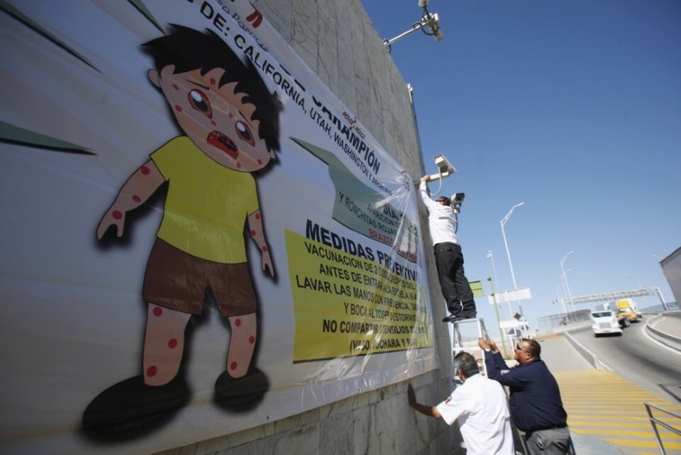 A worker (top) places a banner for a measles prevention programme during an awareness campaign by health workers at the Ciudad Juarez Mexican border crossing with El Paso, Texas  February 16, 2015. (Reuters Photo/Jose Luis Gonzalez)
