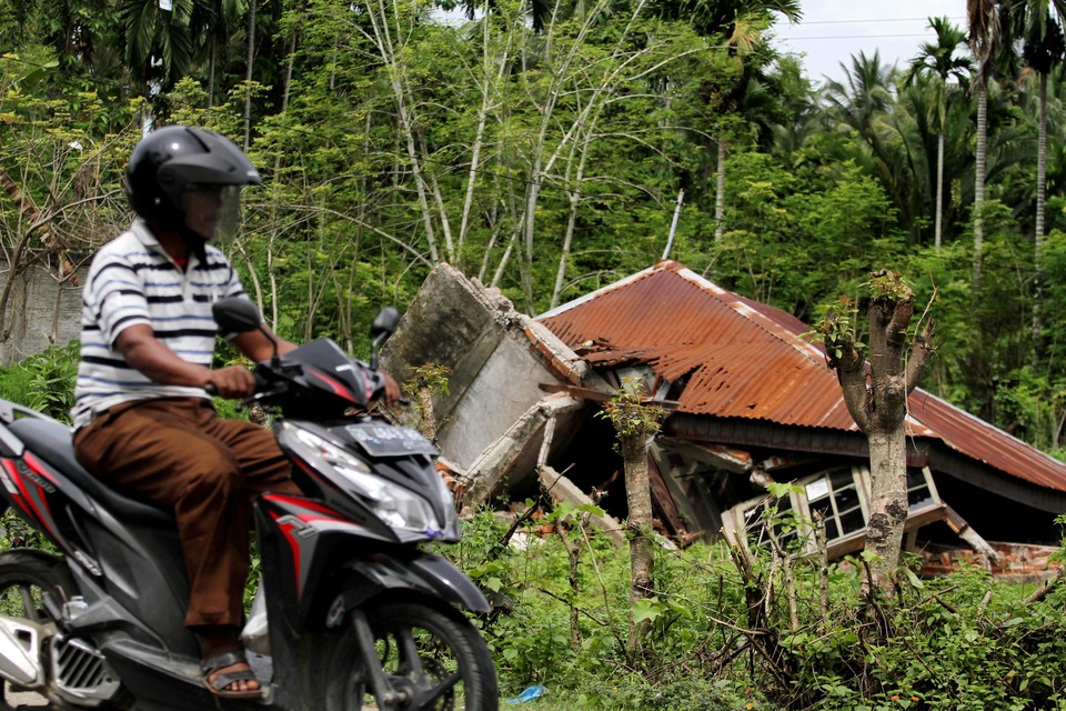 A motorcyclist passes a collapsed house struck by a 6.5 magnitude earthquake in Bandar Baru, Pidie Jaya, Aceh on Monday (26/12). The government has undertaken to reconstruct houses damaged by the earthquake by providing funds to victims worth Rp 40 million ($2972) for homes that are severely damaged and Rp 20 million for homes that have minor damages. (Antara Photo/Rahmat)