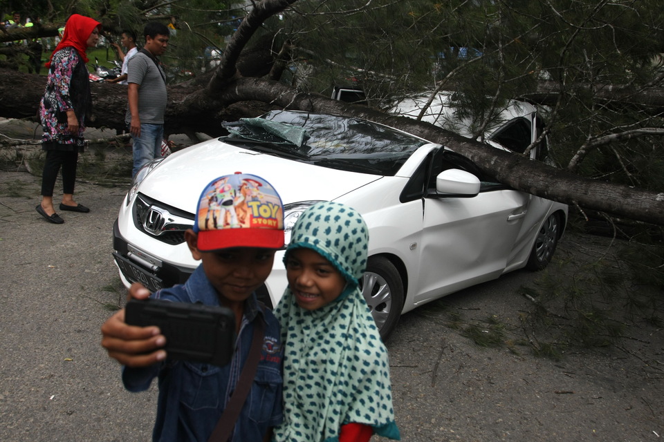Kids take a selfie in front of a car smashed by a fallen tree during a thunderstorm in Kendari, Southeast Sulawesi, on Friday (03/02). (Antara Photo/Jojon)