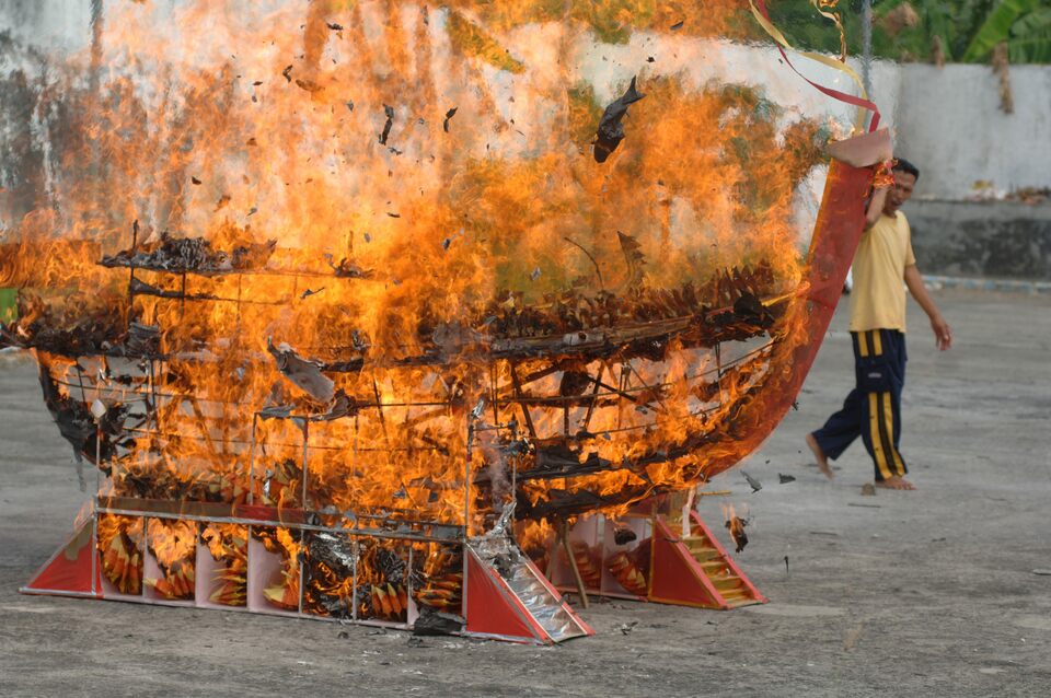 A man passes a burning replica of a ship at the Avalokitesvara Monastery in Pamekasan, East Java, on Tuesday (11/07). The ritual, performed to obtain salvation and success in life, coincides with the commemoration of  Kwan Im, or 'Goddess of Mercy,' the East Asian bodhisattva associated with compassion, as venerated by Mahayana Buddhists. (Antara Photo/Saiful Bahri)