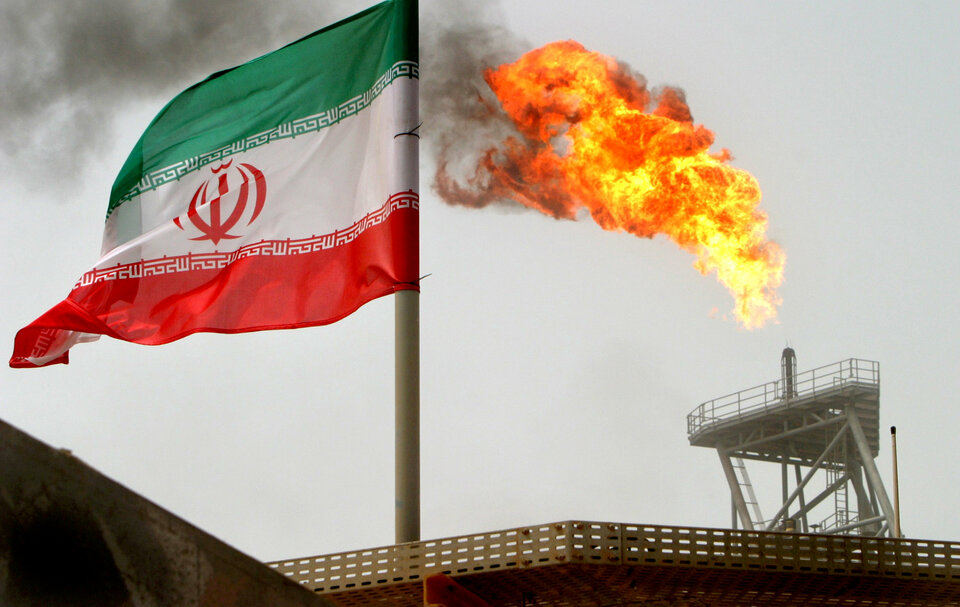 A gas flare on an oil production platform in the Soroush oil fields is seen alongside an Iranian flag in the Gulf July 25, 2005. (Reuters Photo/Raheb Homavandi)