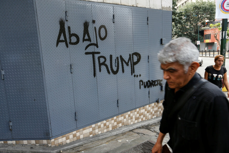 A man walks past a graffiti in Caracas, Venezuela, Sunday (13/08). The graffiti reads: 'Down with Trump ... Rot.' (Reuters Photo/Andres Martinez Casares)