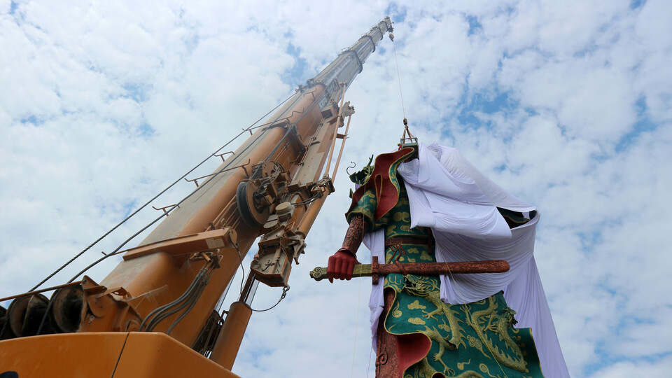 Members of the Regional Disaster Management Agency (BPBD) in Tuban, East Java, using a crane to lower a canvas over the statue of Kongco Kwan Sing Tee Koen at Kwan Swie Bio Temple on Sunday (06/08). The temple board was forced to cover the 30.4-meter-tall statue after objections by certain groups. (Antara Photo/Aguk Sudarmojo)