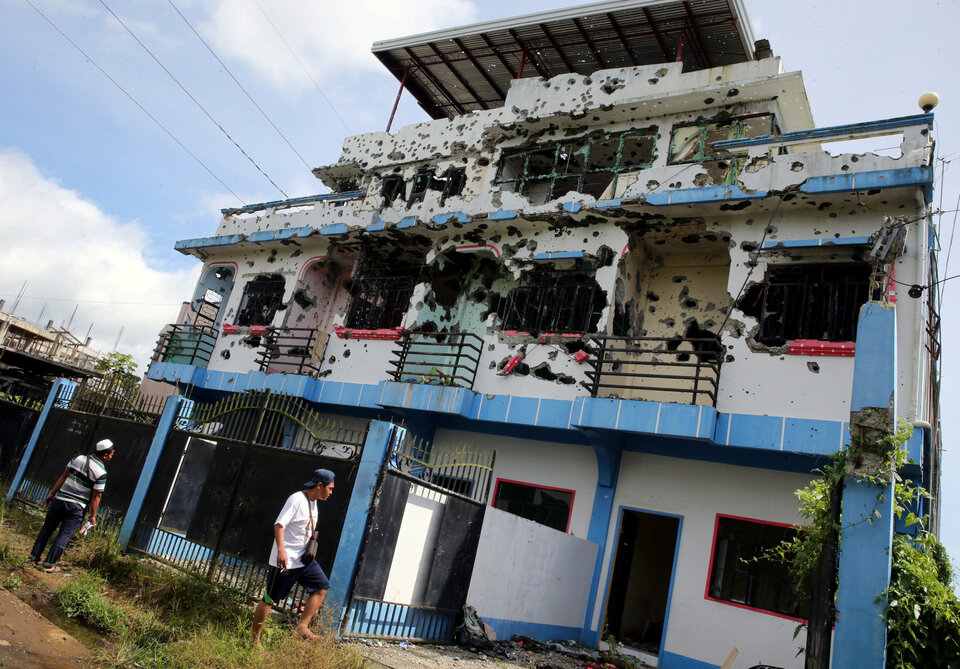 People walk in front of a bullet-riddled apartment house in a residential area in Malutlut district, Marawi city, southern Philippines Friday (27/10), which was believed to have been rented by pro-Islamic State militant group leaders Isnilon Hapilon and Omar Maute before their battle in Marawi city.  (Reuters Photo/Romeo Ranoco)