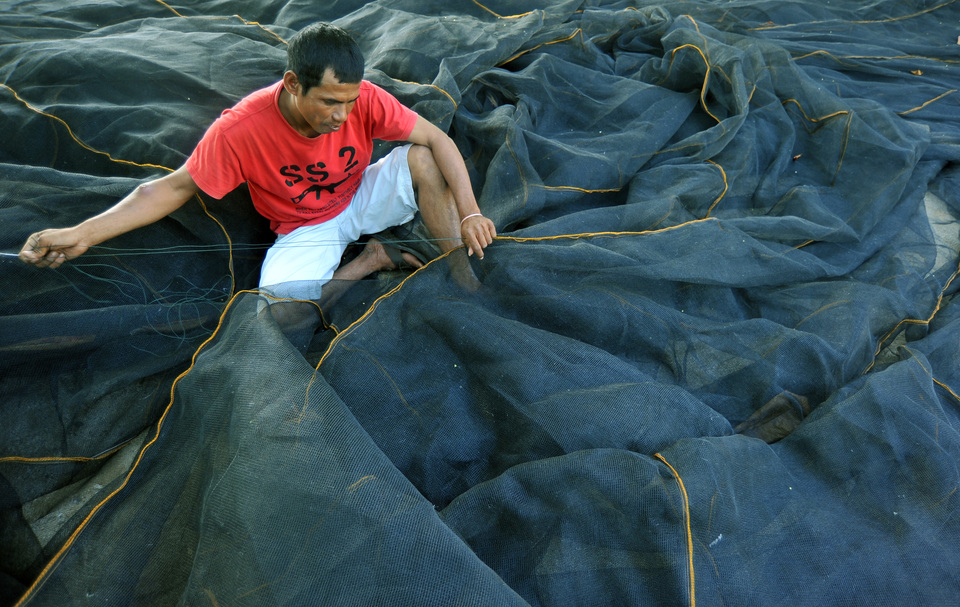 A fisherman sews a net to be used on his barge in Padang, West Sumatra, on Tuesday (17/10). (Antara Photo/Iggoy el Fitra)

