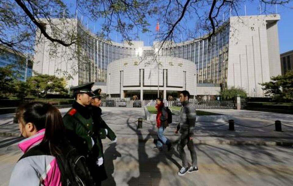 People walk past the headquarters of the People's Bank of China (PBOC), the central bank, as two paramilitary police officials patrol around it in Beijing.   (Reuters Photo/Jason Lee)