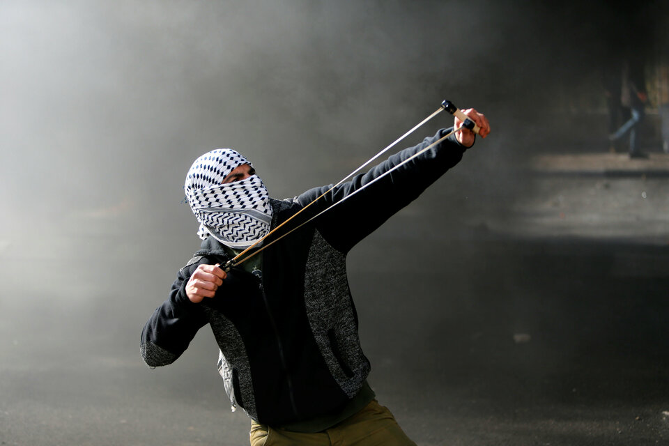 A Palestinian protester uses a sling shot to hurl stones towards Israeli troops during clashes as Palestinians call for a "day of rage" in response to US President Donald Trump