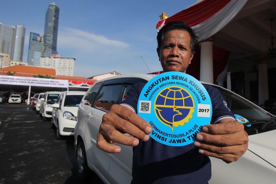 A taxi driver displays a sticker containing his data and that of his vehicle during the inauguration of special permits for online-based transportation services in Surabaya, East Java, on Thursday (04/01). More than 110 drivers have obtained operating permits from the provincial department of transportation. (Antara Photo/Didik Suhartono)