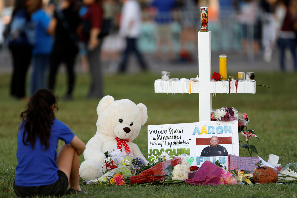 A mourner sits by a cross adorned with pictures of victims, along with flowers and other mementos, at a memorial two days after the shooting at Marjory Stoneman Douglas High School in Parkland, Florida, Feb. 16.  (Reuters Photo/Jonathan Drake)