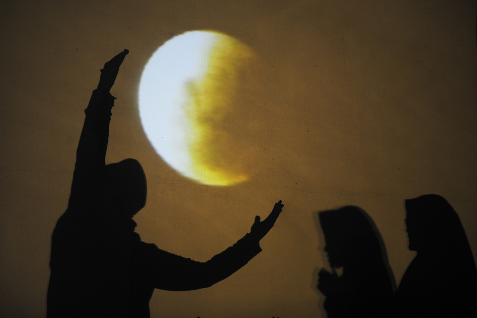 A woman strikes a pose in front of a screen displaying the 'super blue blood moon' lunar eclipse at Al-Akbar Mosque in Surabaya, East Java, on Wednesday evening (31/01). (Antara Photo/Zabur Karuru)