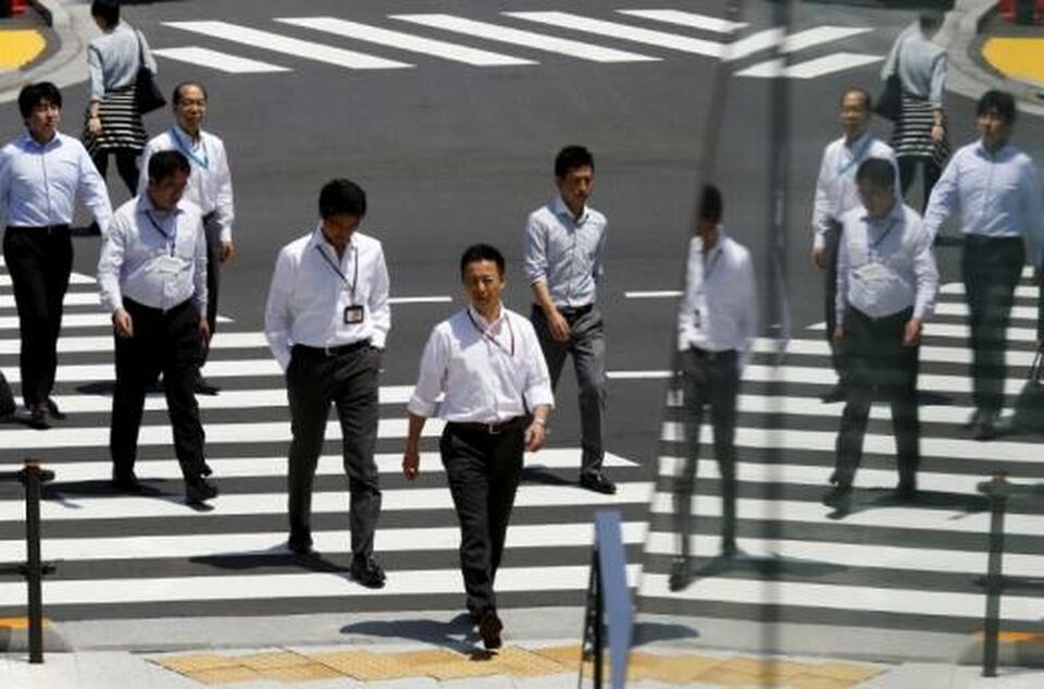 Office workers are reflected in a glass railing as they cross a street during lunch hour in Tokyo. (Reuters Photo/Thomas Peter)