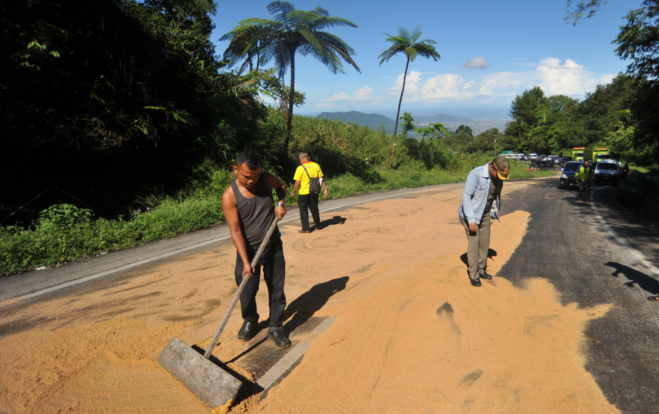 Officials and residents cover a palm oil spill with rice husks on Jalan Raya Padang-Solok in Padang, West Sumatra, on Monday (02/04). The oil leaked from a truck after an accident, making the road's surface dangerously slippery. (Antara Photo/Iggoy el Fitra)