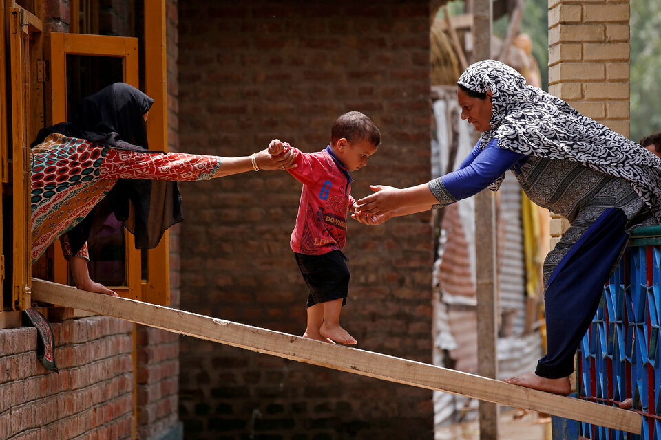 Women help a child to cross over to the other house on a wooden plank after flash floods in Tailbal, on the outskirts of Srinagar in the Indian state of Jammu and Kashmir, on July 24, 2018. (Reuters Photo/Danish Ismail)