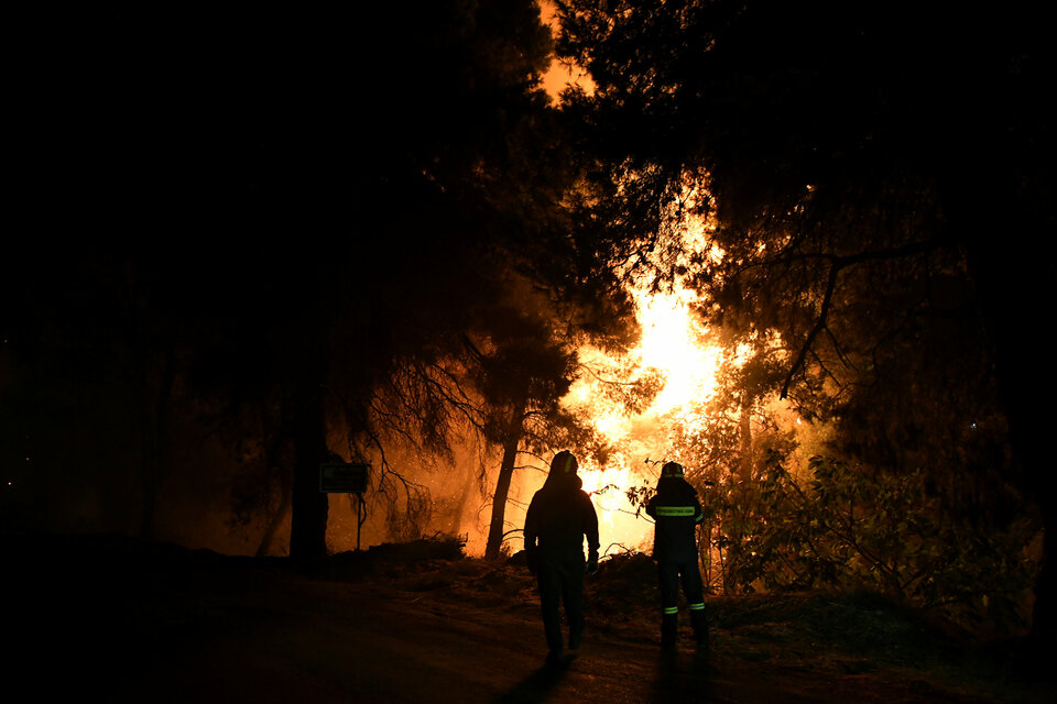 Firefighters looks at rising flames during a wildfire near the village of Psahna, in Evia, Greece, Sunday (12/08). (Reuters Photo/Michalis Karagiannis)