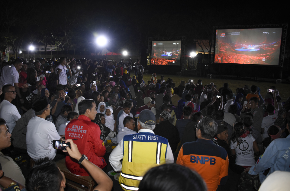 President Joko 'Jokowi' Widodo, third from left, accompanied by West Nusa Tenggara Governor Zainul Majdi, second from left, watch the closing ceremony of the 2018 Asian Games with earthquake victims in Gunungsari, West Lombok district, West Nusa Tenggara, on Sunday evening (02/09). (Antara Photo/Ahmad Subaidi)