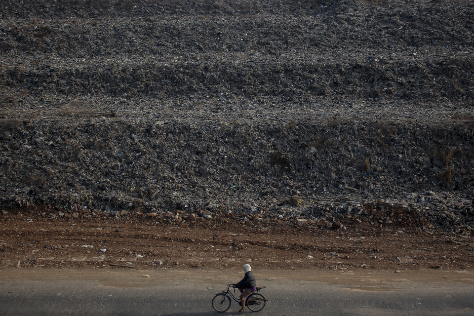 A cyclist is dwarfed by the Rawa Kucing landfill in Tangerang, Banten, on Thursday. The millions of tons of waste dumped in the area have piled up to a height of 18 meters over the past 26 years, because the facility lacks a garbage shredder. (Antara Photo/Fauzan)