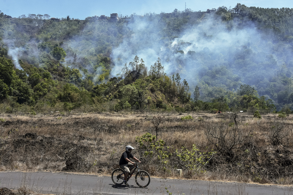 A cyclist rides past a burning forest near Batur village in Kintamani, Bali, on Sunday. The fire reportedly broke out at a tourism site near Mount Batur on Saturday afternoon. (Antara Photo/Nyoman Hendra Wibowo)