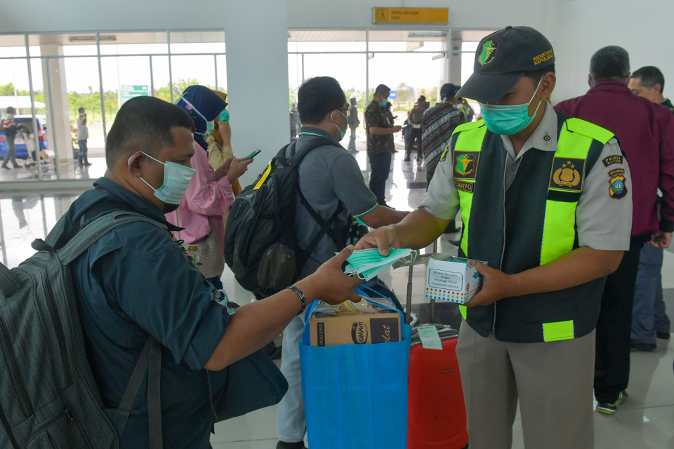 An officer distributes masks to passengers at Raden Sadjad Airport in Ranai, Natuna – where the Wuhan evacuees are being quarantined – on Tuesday. (Antara Photo/M. Risyal Hidayat)