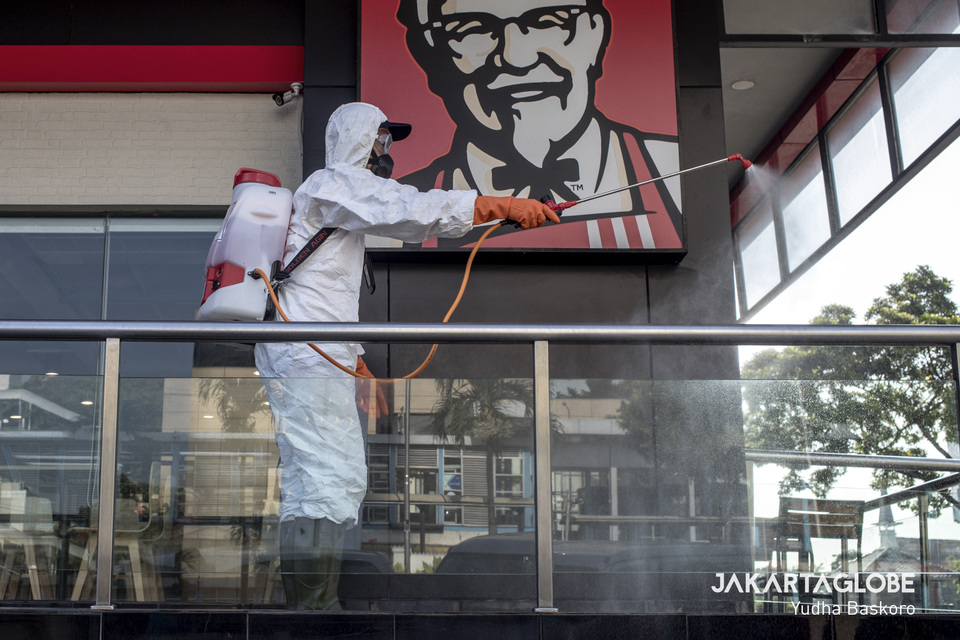 An Indonesian Red Cross personnel wearing protective gear sprays a KFC sign with disinfectant at the Sarinah department store in Central Jakarta on Tuesday. (JG Photo/Yudha Baskoro)