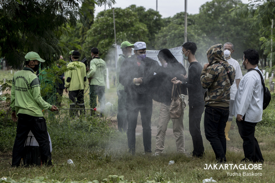 A funeral service worker sprays a family attending the burial of a suspect Covid-19 patient with disinfectant at Tegal Alur cemetery in West Jakarta on Thursday. (JG Photo/Yudha Baskoro)