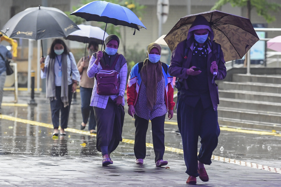 Jakartans heed the government's instruction to wear masks to prevent the spread of coronavirus as they walk in the rain in Central Jakarta on Monday. (Antara Photo/Muhammad Adimaja)