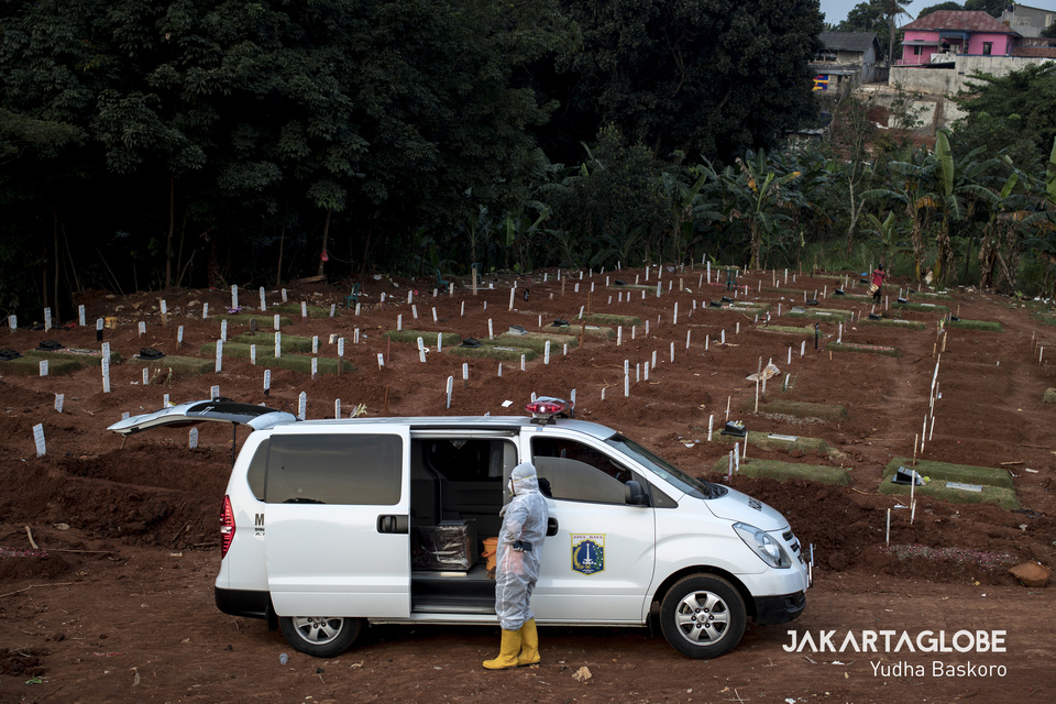 A funeral service worker stands outside an ambulance carrying the body of a Covid-19 victim at Pondok Ranggon public cemetery in East Jakarta on Wednesday. (JG Photo/Yudha Baskoro)