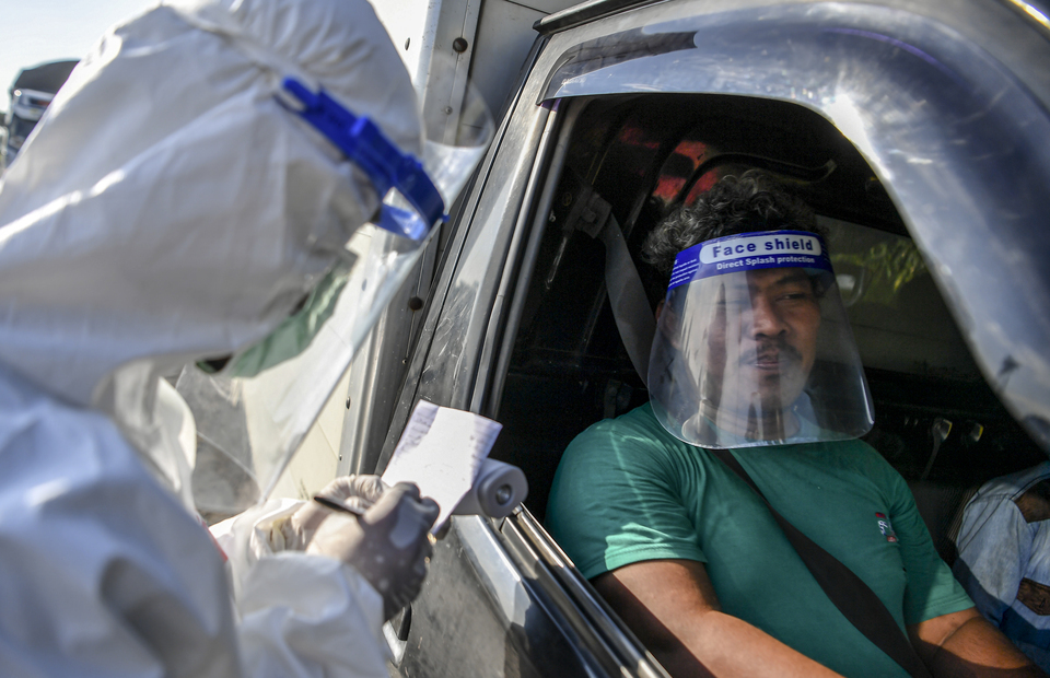 An official in hazmat suit checks a traveler's travel documents on Jalan Raya Pantura in Cirebon, West Java, on May 19. (Antara Photo/Nova Wahyudi)