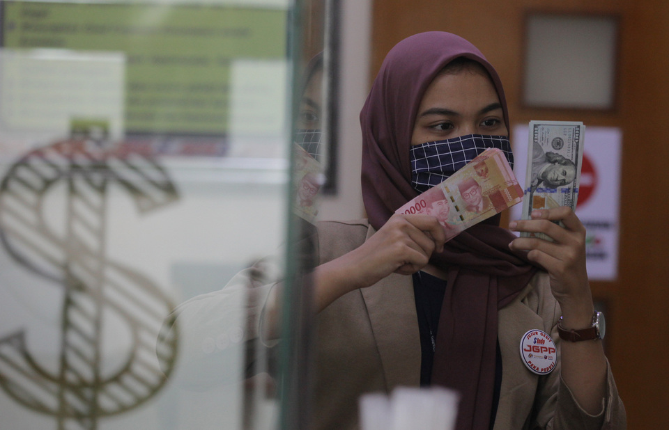 An employee displays Indonesian rupiah and US dollars at a foreign currency exchange booth in Jakarta. (ANTARA FOTO/Reno Esnir).
