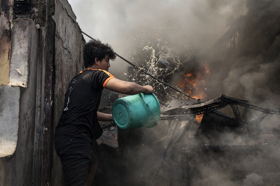 A man throws a bucket of water on a burning building during a fire in Manggarai, South Jakarta on Tuesday. (JG Photo/Yudha Baskoro)