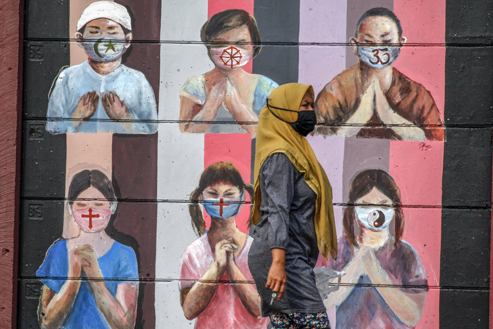 A woman walks in front of a mural encouraging the wearing of masks during the Covid-19 pandemic on Jalan Juanda, Depok, West Java, on June 18, 2020. (Antara Photo/Yulius Satria Wijaya)