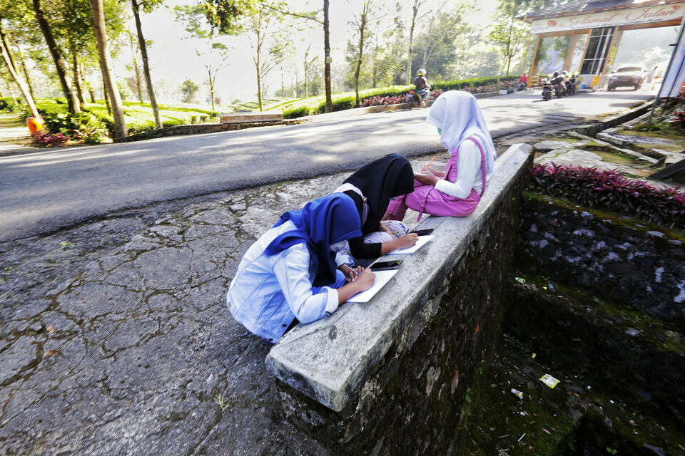 Junior high school students do their online homework at the roadside in search for better internet signal in Gunung Mas area, Bogor, West Java, on July 28, 2020. Most schools in Indonesia apply remote learning during the Covid-19 pandemic. (Beritasatu Photo/Ruht Semiono)