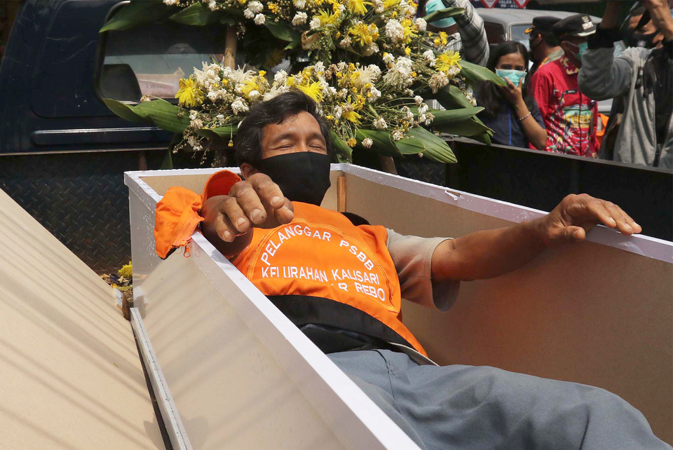A man is ordered to lay in a coffin as punishment for not wearing a mask in Pasar Rebo, East Jakarta on Sept. 3, 2020. (Beritasatu Photo/Joanito De Saojoao)