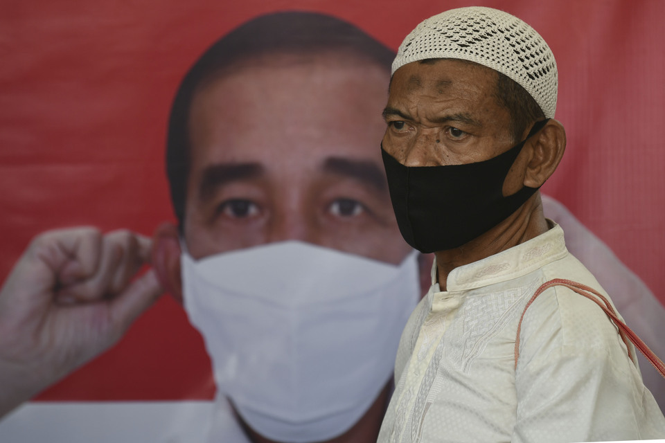 This 2020 file photo shows a man wearing a mask walking in front of a Jokowi poster at Tanah Abang Train Station in Jakarta. (Antara Photo/M. Risyal Hidayat)