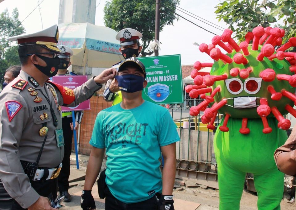 A police officer put face mask on a man at Tangerang Train Station in Tagerang, Banten during a city-wide mask wearing campaign last Thursday. (Antara Photo/Muhammad Iqbal)