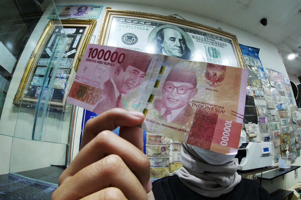 This 2020 file photo shows worker at a money changer shop in Jakarta holds up a Rp 100,000 banknote. (Investor Daily/David Gita Roza)