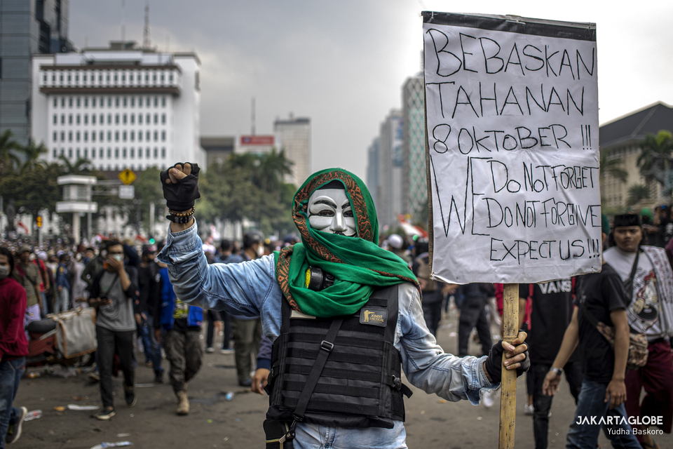 A protester wearing a Guy Fawkes mask carries a placard during a riot near Arjuna Wijaya Statue, also affectionally known as the Horse Statue, in Central Jakarta on Tuesday. (JG Photo/Yudha Baskoro)