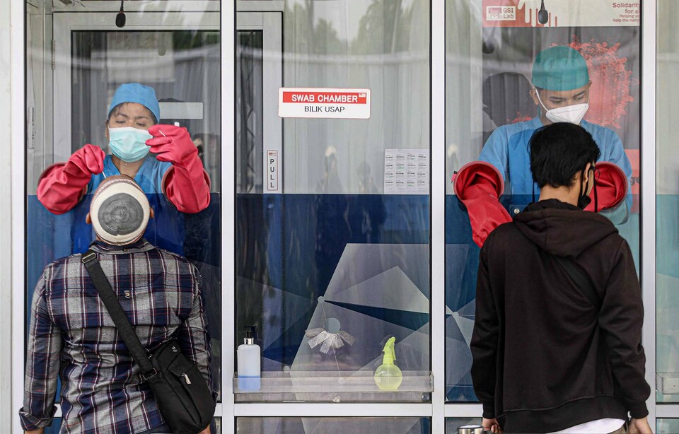 Medical workers take specimen from residents for coronavirus tests from behind a glass screen at a laboratory in Cilandak, South Jakarta, on Oct. 26, 2020. (Beritasatu Photo/Joanito De Saojoao)