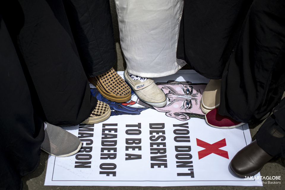 Protesters stand on a poster with a caricature of French President Emmanuel Macron in front of the Embassy of France building in Central Jakarta on Monday. (JG Photo/Yudha Baskoro)