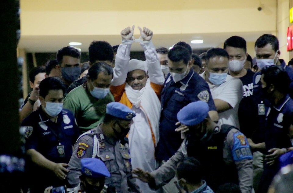 Rizieq Syihab raises his cuffed hands as he is being escorted to the detention facility as a suspect in health protocol violation case on Dec. 13, 2020. The Islamic Defenders Front (FPI) leader is detained  after 11-hour interrogation at the Jakarta Police headquarters. (Beritasatu Photo/Joanito De Saojoao)