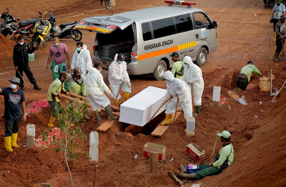 Funeral workers lower the coffin of a Covid-19 victim at Pondok Rangon cemetery in East Jakarta on Sept. 27, 2020. (Beritasatu Photo/Joanito De Saojoao)

.