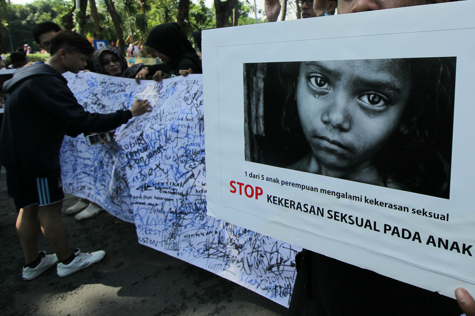 A resident signs a white cloth during a symbolic action against sexual harassment. (ANTARA FOTO/Didik Suhartono)